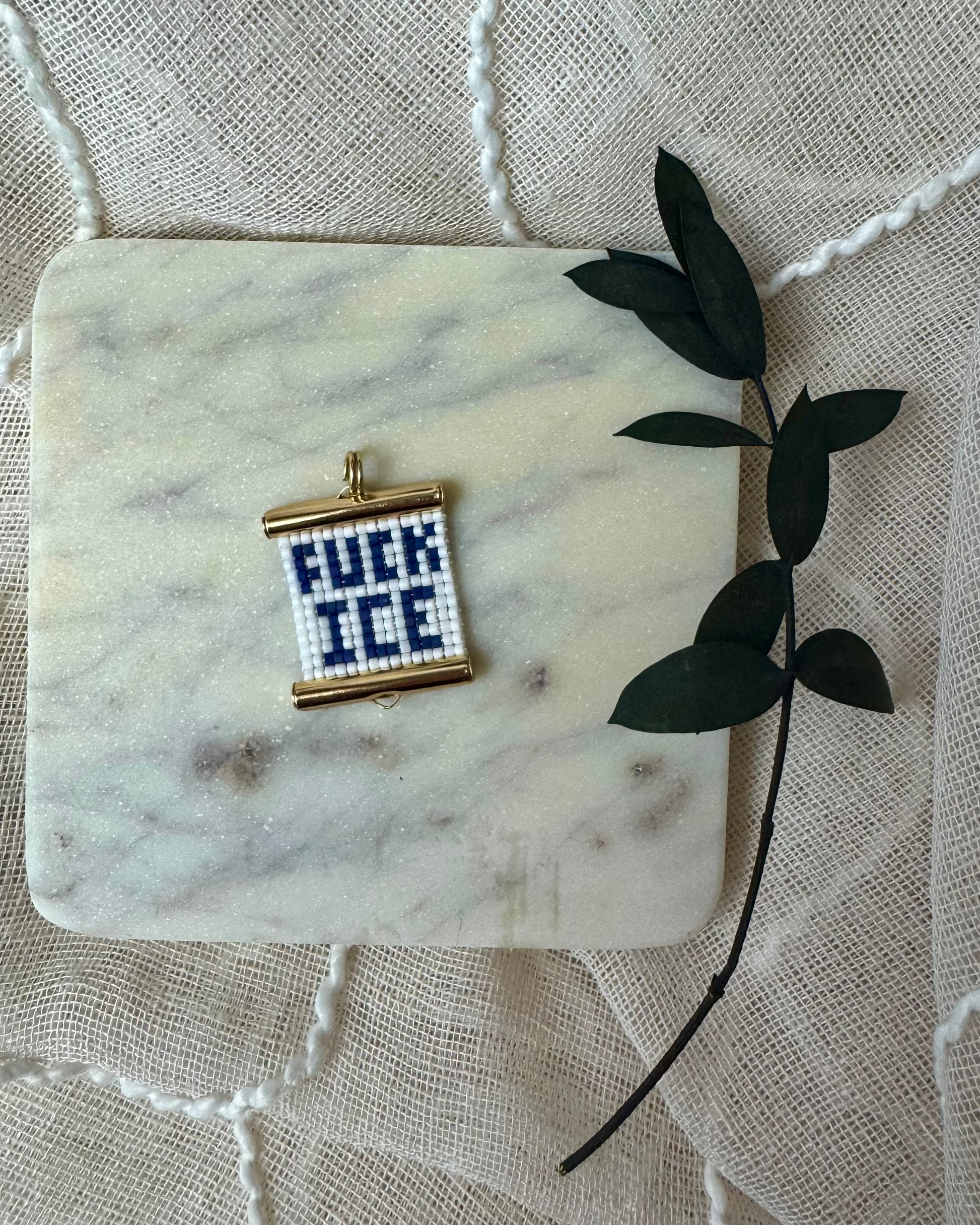 Small beaded charm with text on a marble coaster with a leafy branch.