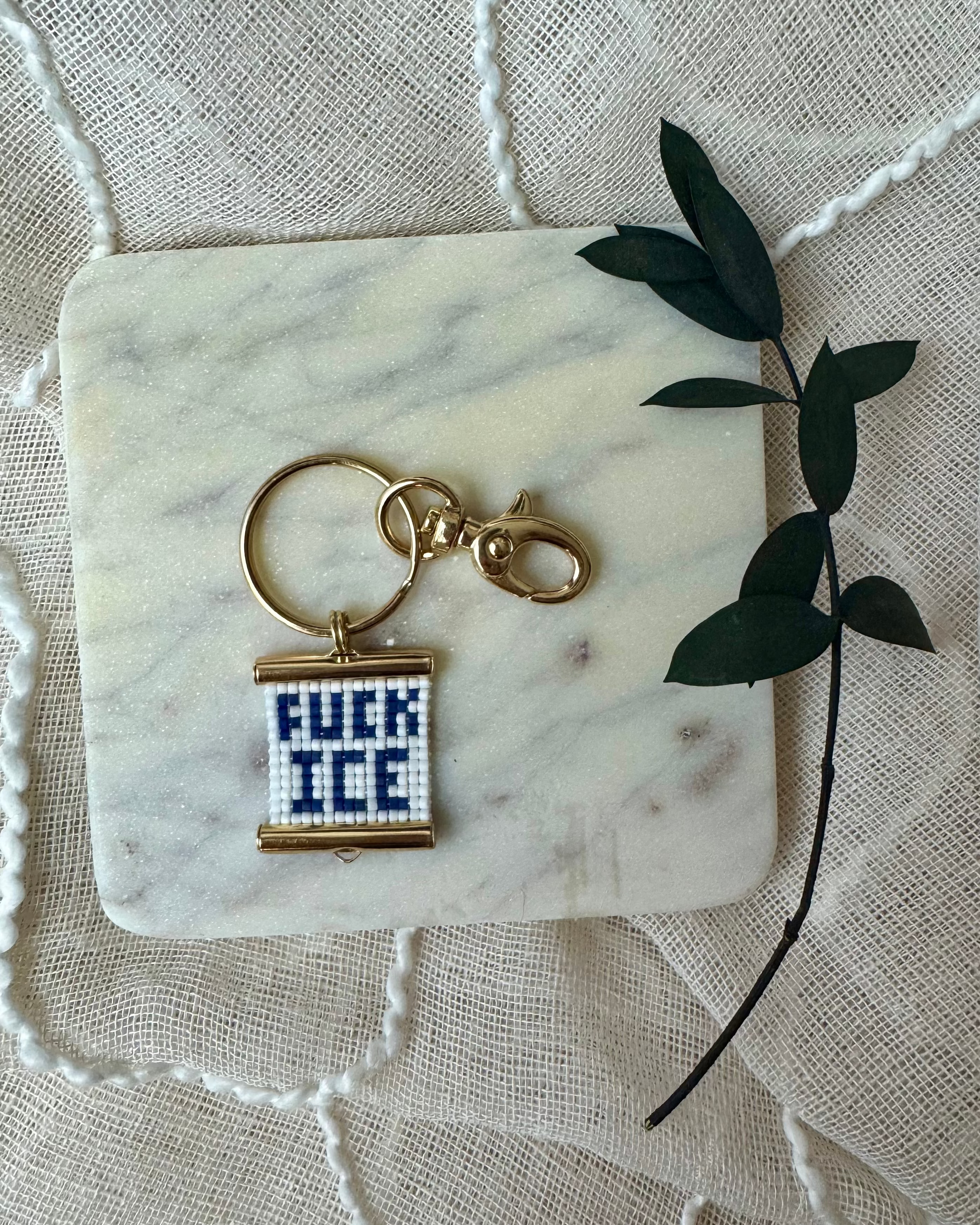 Beaded bag charm with relevant message text on a marble coaster with a leaf decoration.