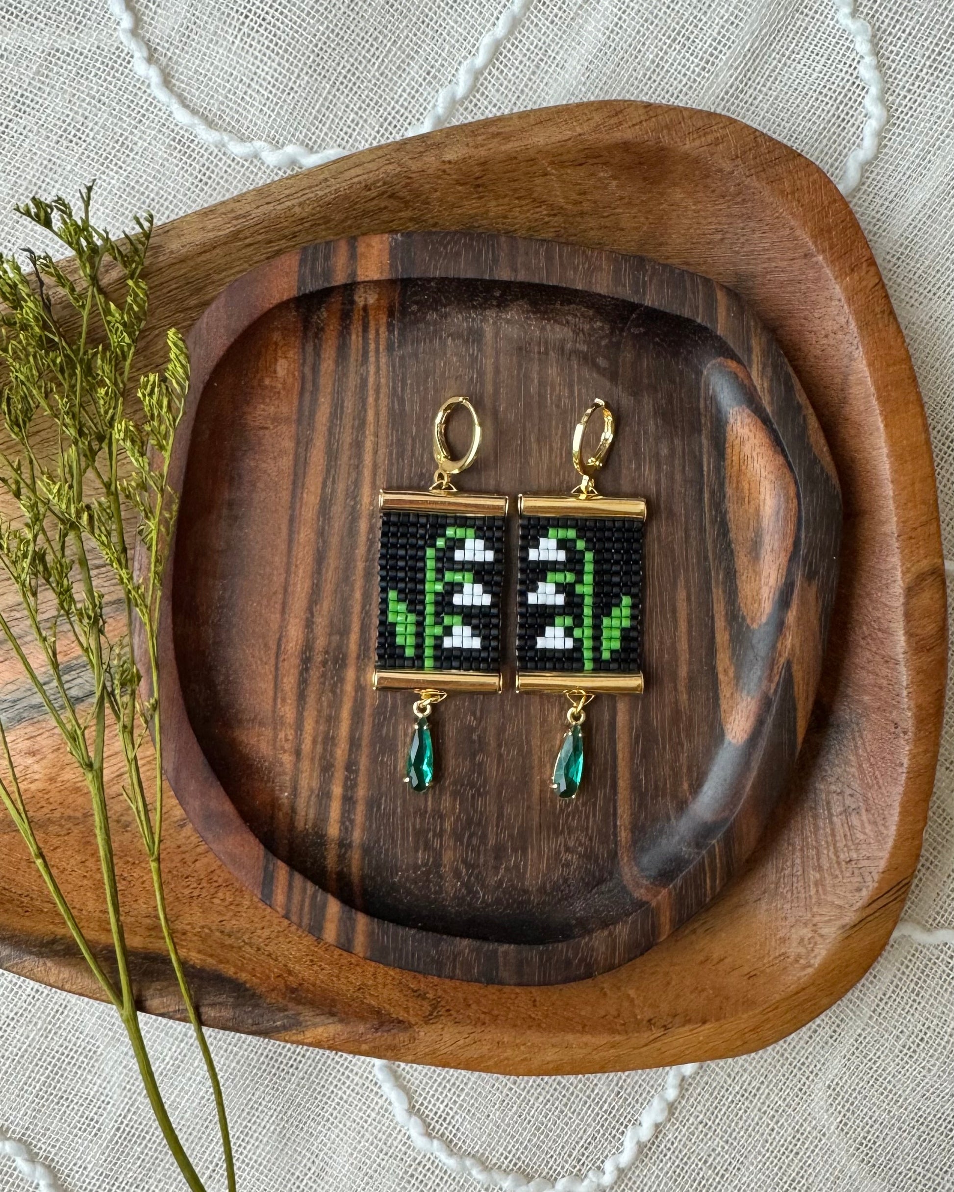 Pair of earrings with floral design on a wooden tray.