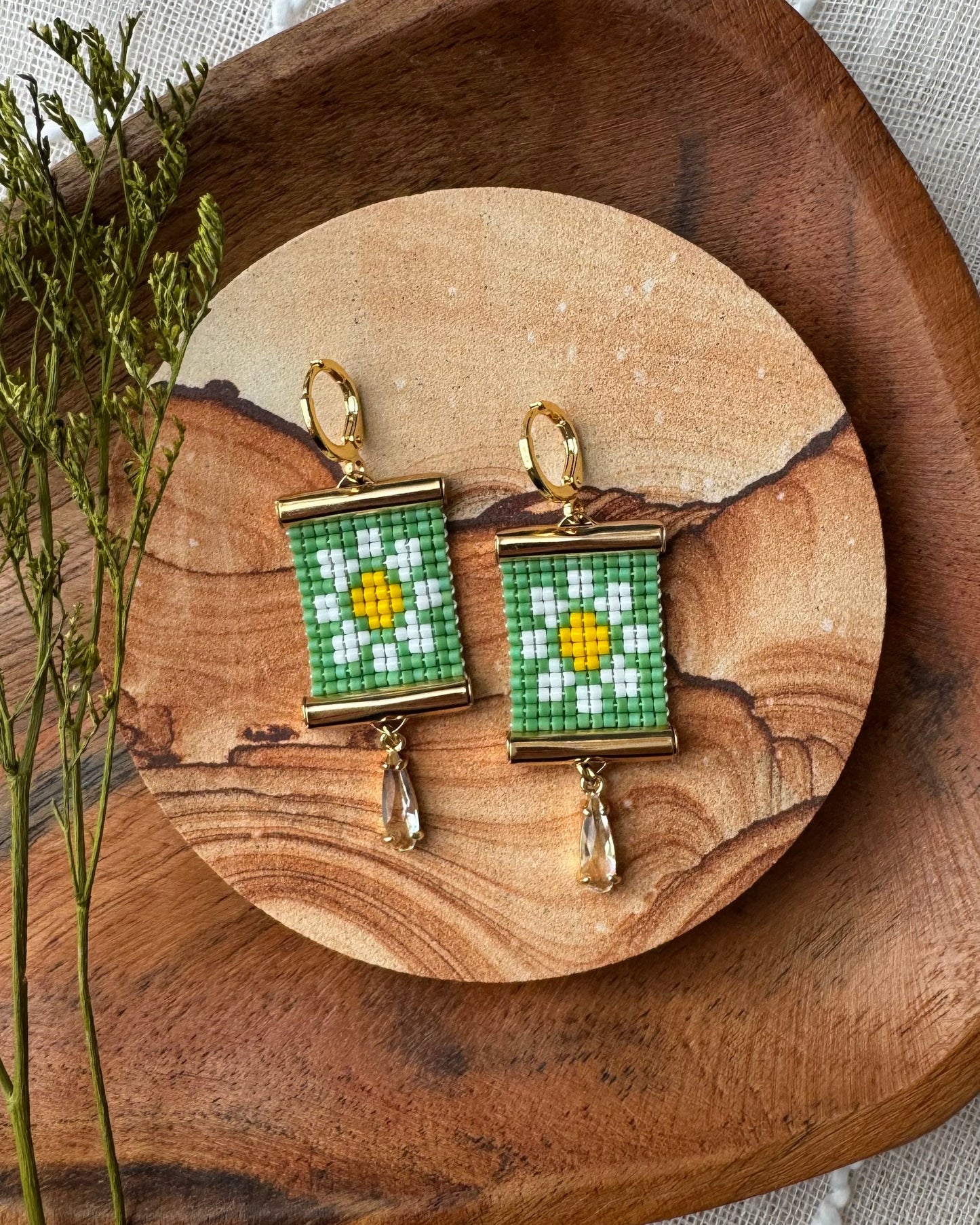 Pair of beaded earrings with a daisy design on a wooden surface with a natural background