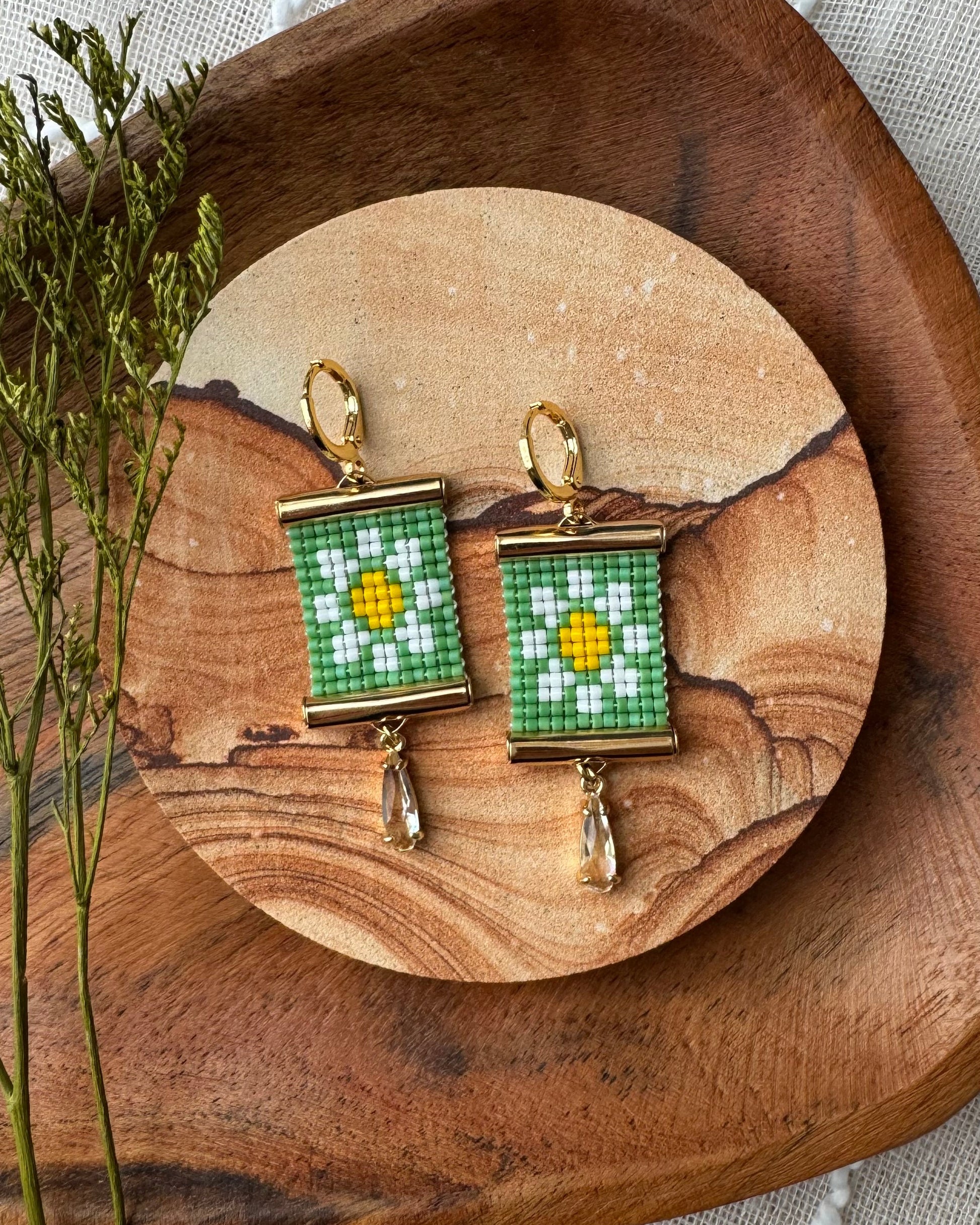 Pair of beaded earrings with a daisy design on a wooden surface with a natural background