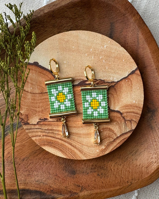 Pair of beaded earrings with a daisy design on a wooden surface with a natural background