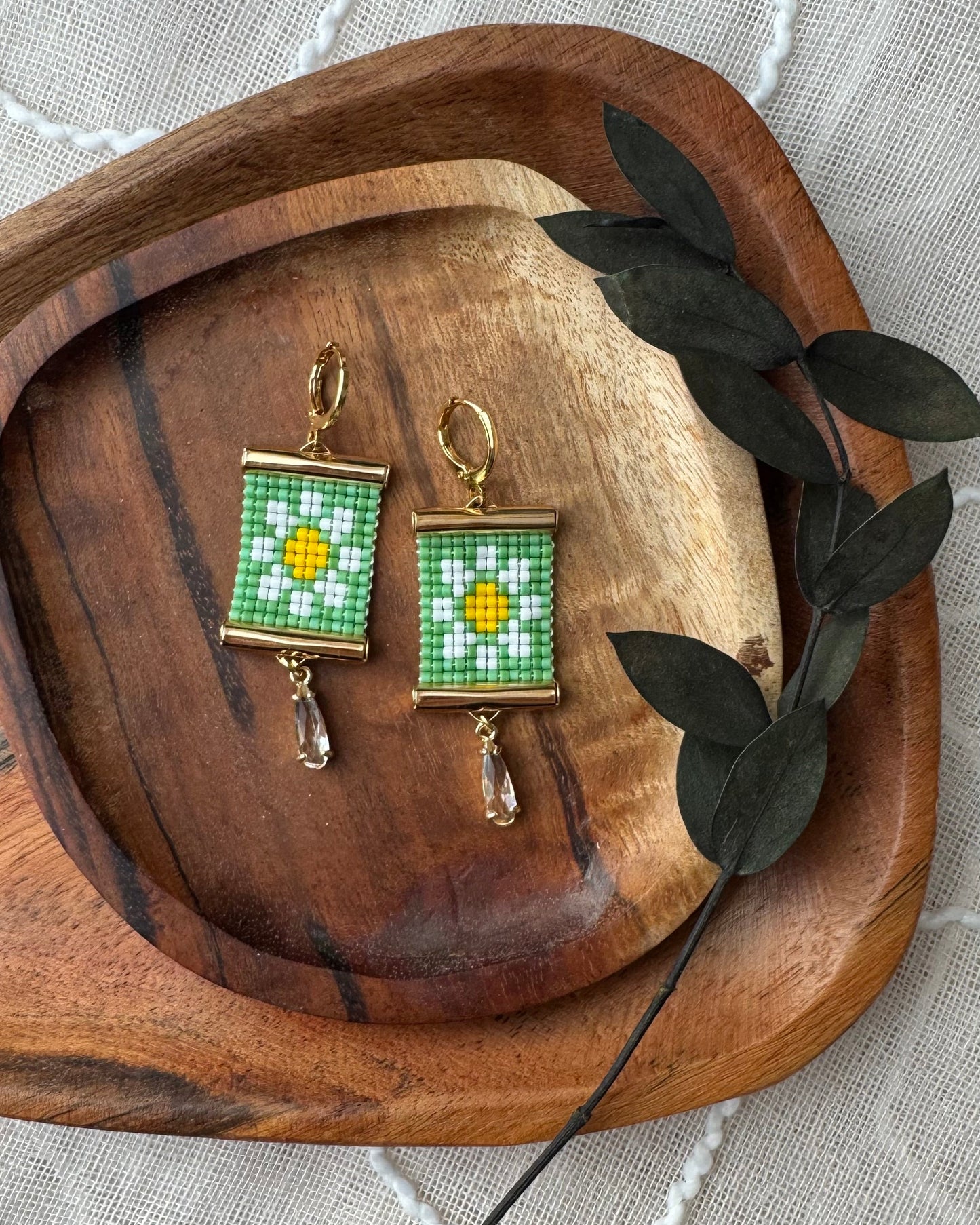 Beaded earrings with floral design on a wooden tray with leaves.