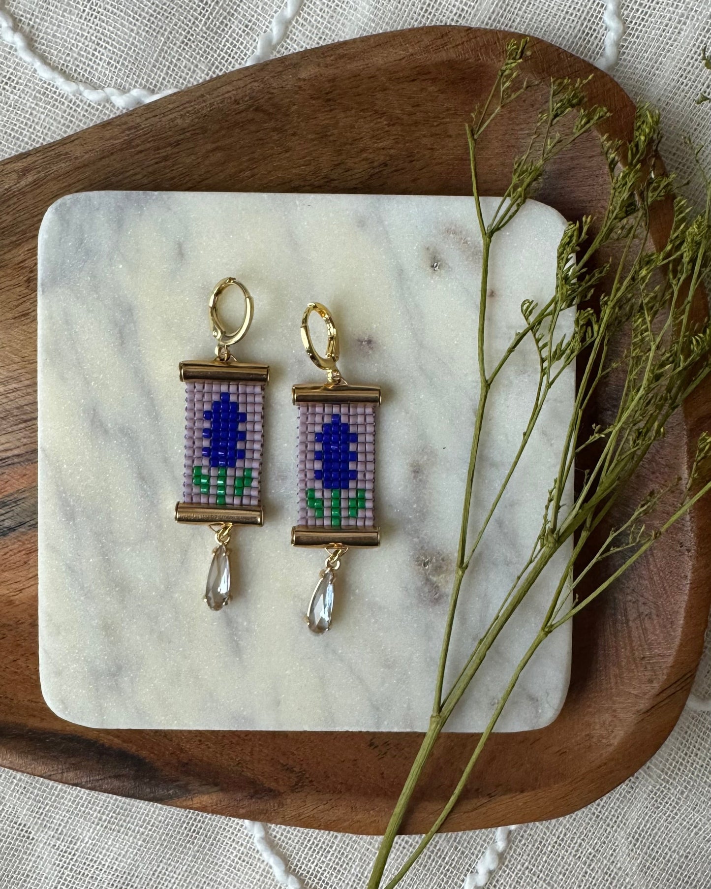Pair of beaded earrings with floral design on a marble coaster with a wooden base.