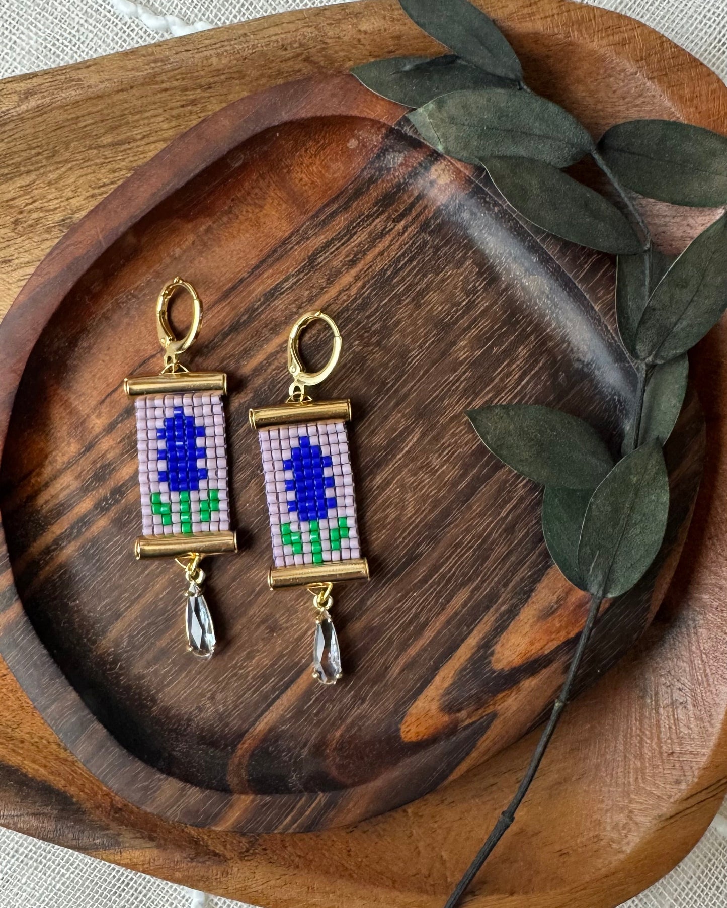 Beaded floral earrings on a wooden tray with green leaves