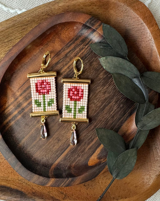 Pair of beaded earrings with rose design on a wooden tray