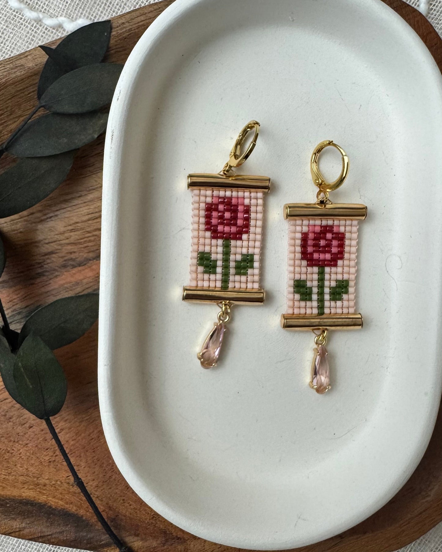 Pair of beaded earrings with rose design on a white dish
