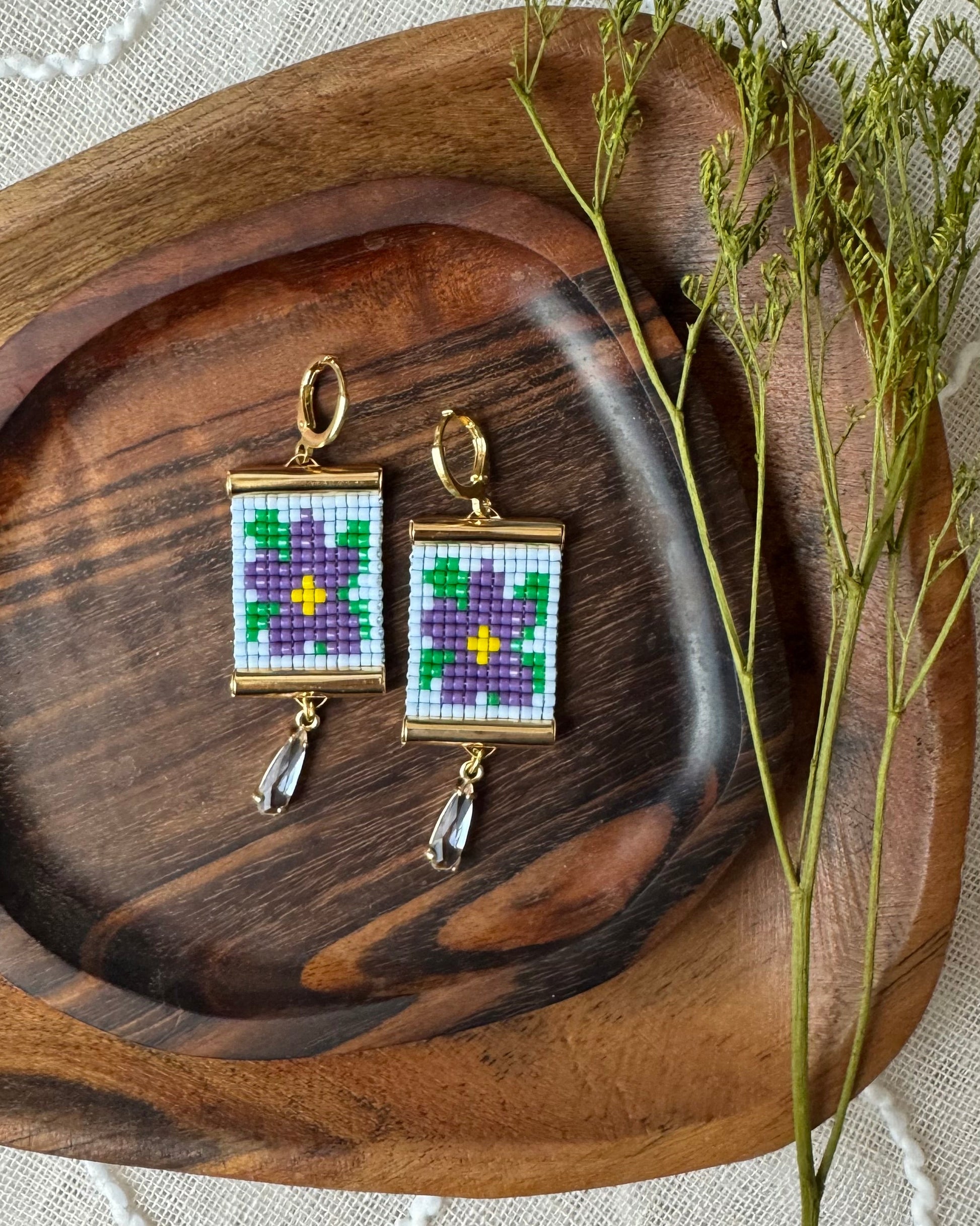Pair of earrings with beaded flower design on a wooden tray