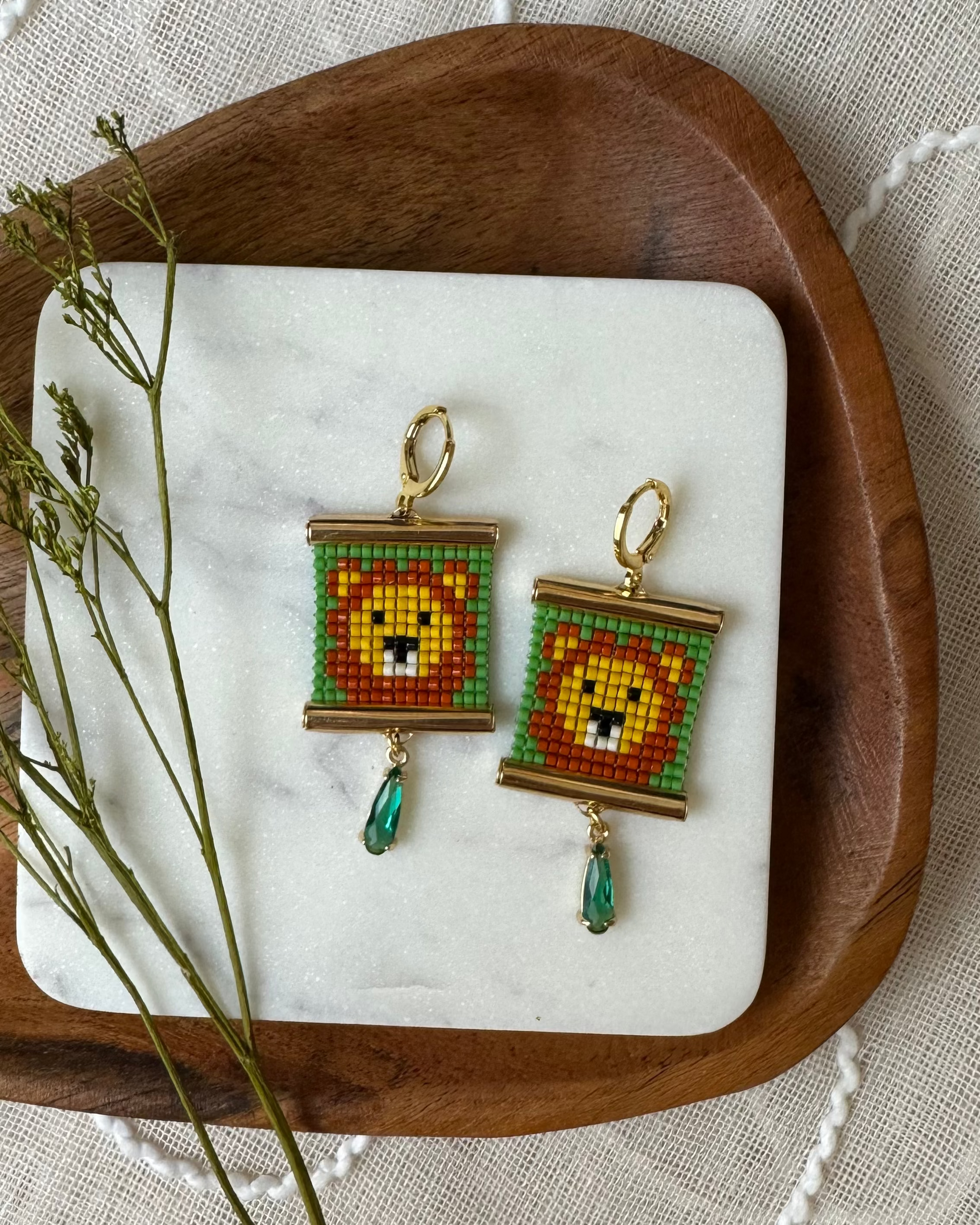 Pair of beaded earrings with lion design on a wooden tray with a white cloth background
