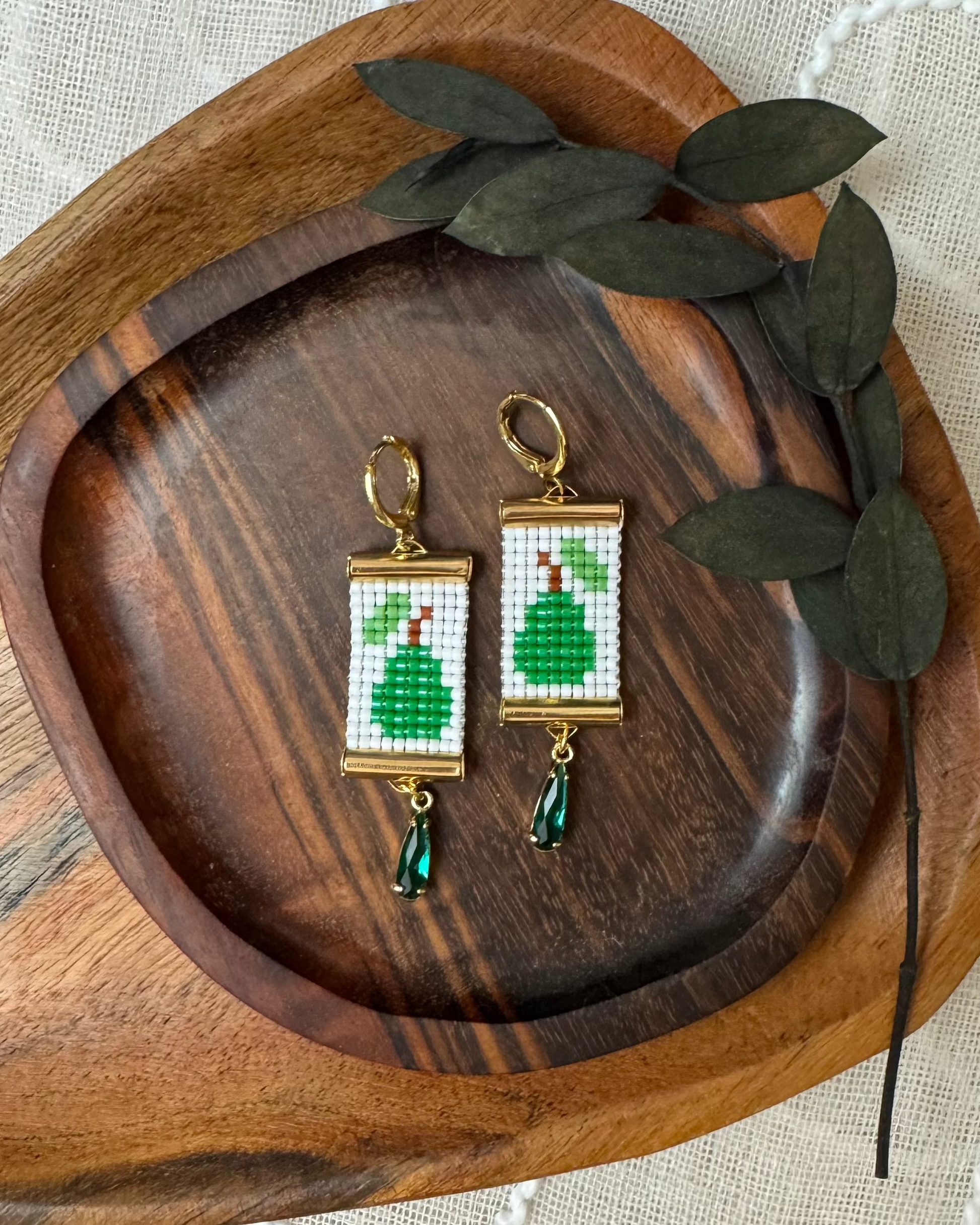 Pair of beaded earrings with green pear design on a wooden tray with leaves.
