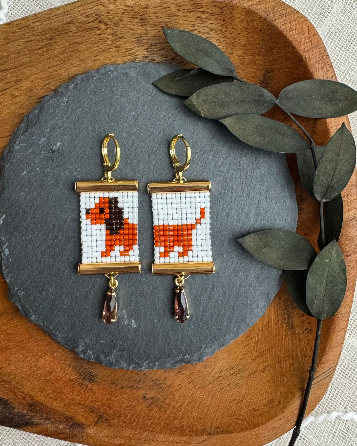 Pair of earrings with beaded daschund design on a wooden tray with leaves.