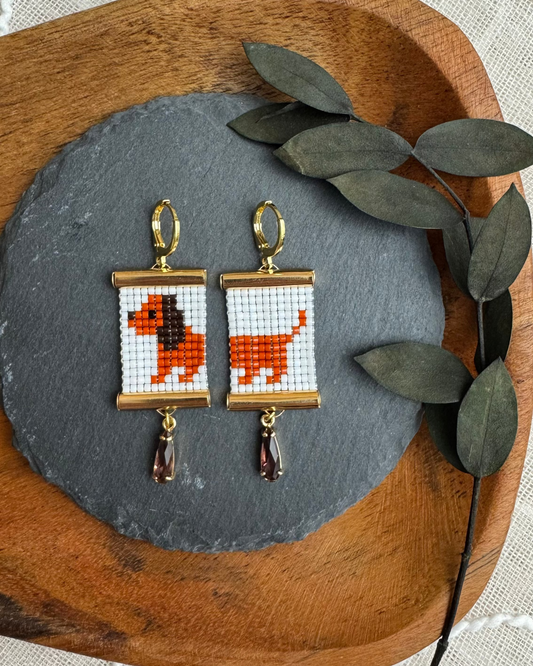 Pair of earrings with beaded daschund design on a wooden tray with leaves.