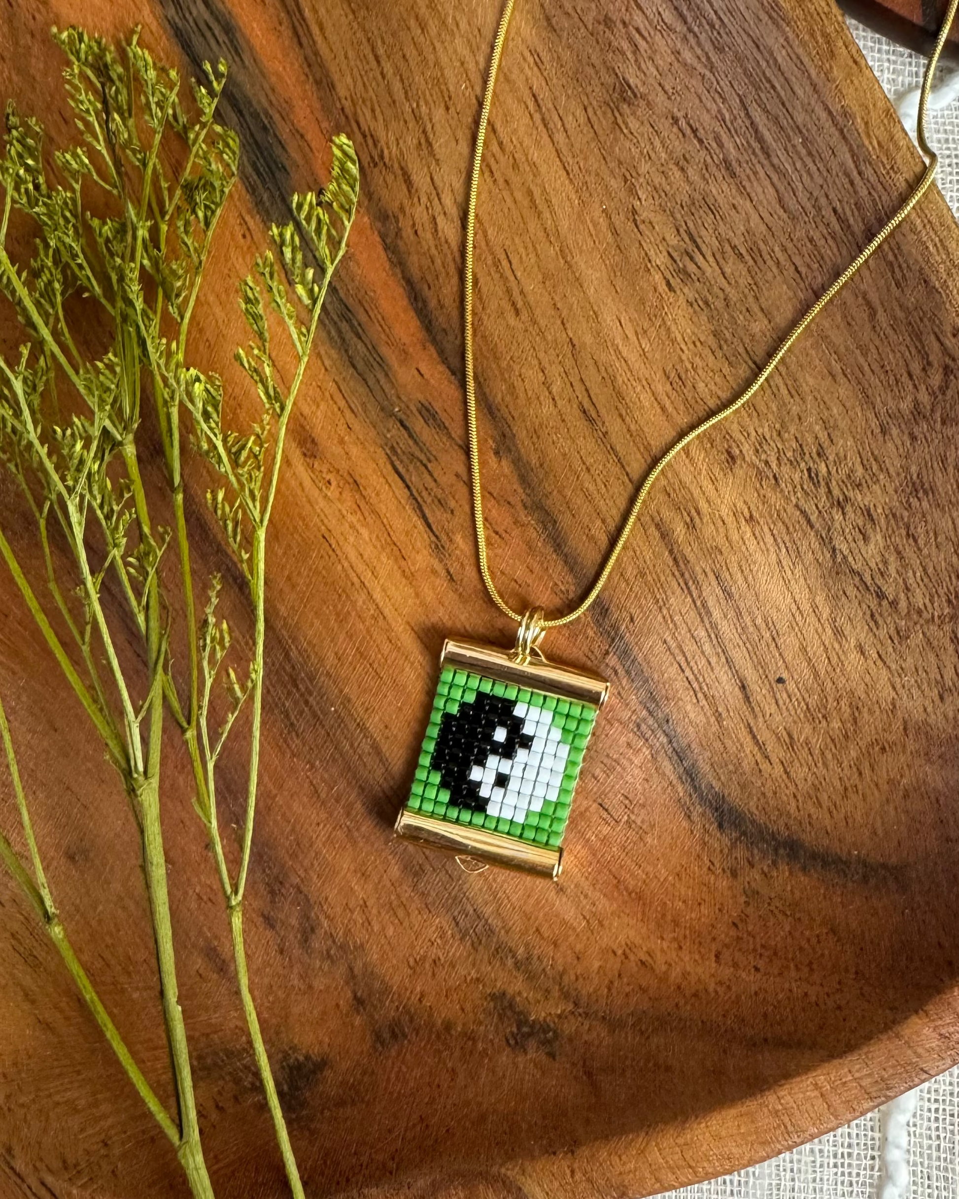 Necklace with a square pendant featuring a black and white design on a wooden surface with green leaves.