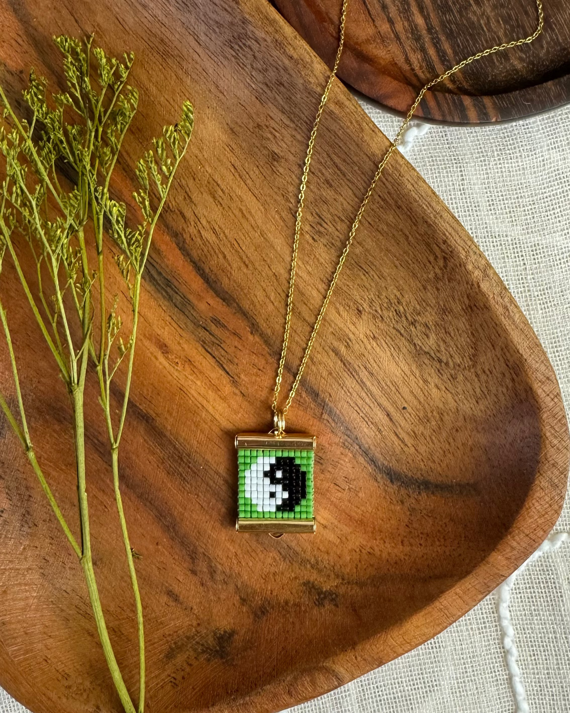 Necklace with a beaded pendant featuring a yin yang symbol on a wooden surface.