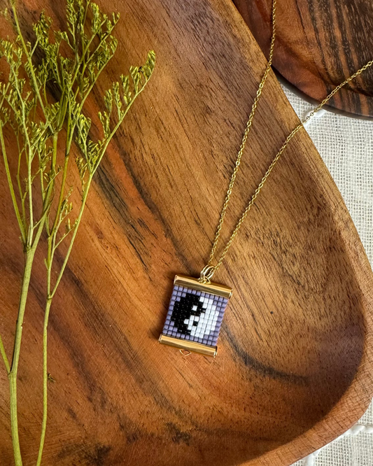 Necklace with a beaded pendant on a wooden surface next to dried plants