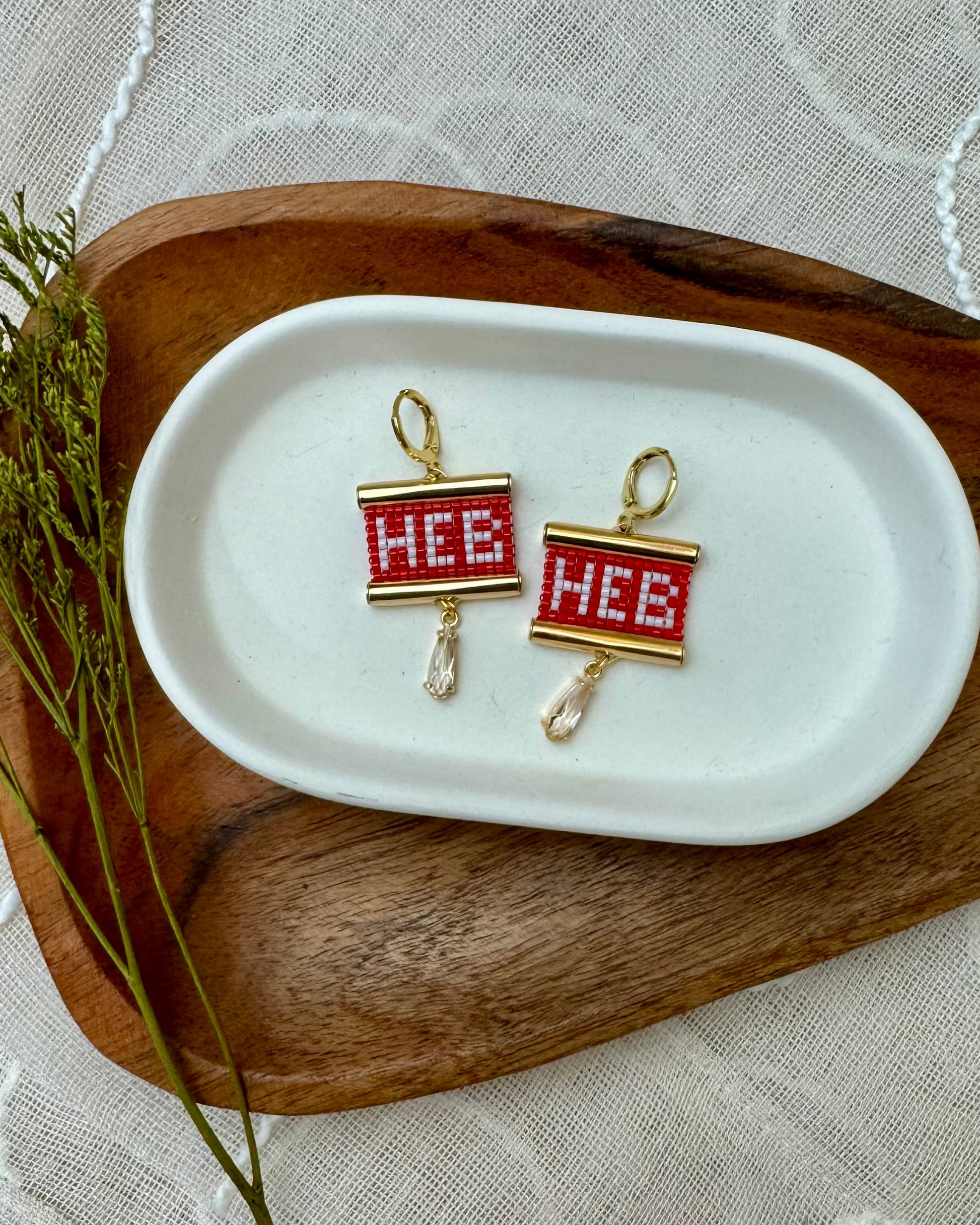 Beaded Earrings with 'HEB' design on a white dish on a wooden surface.