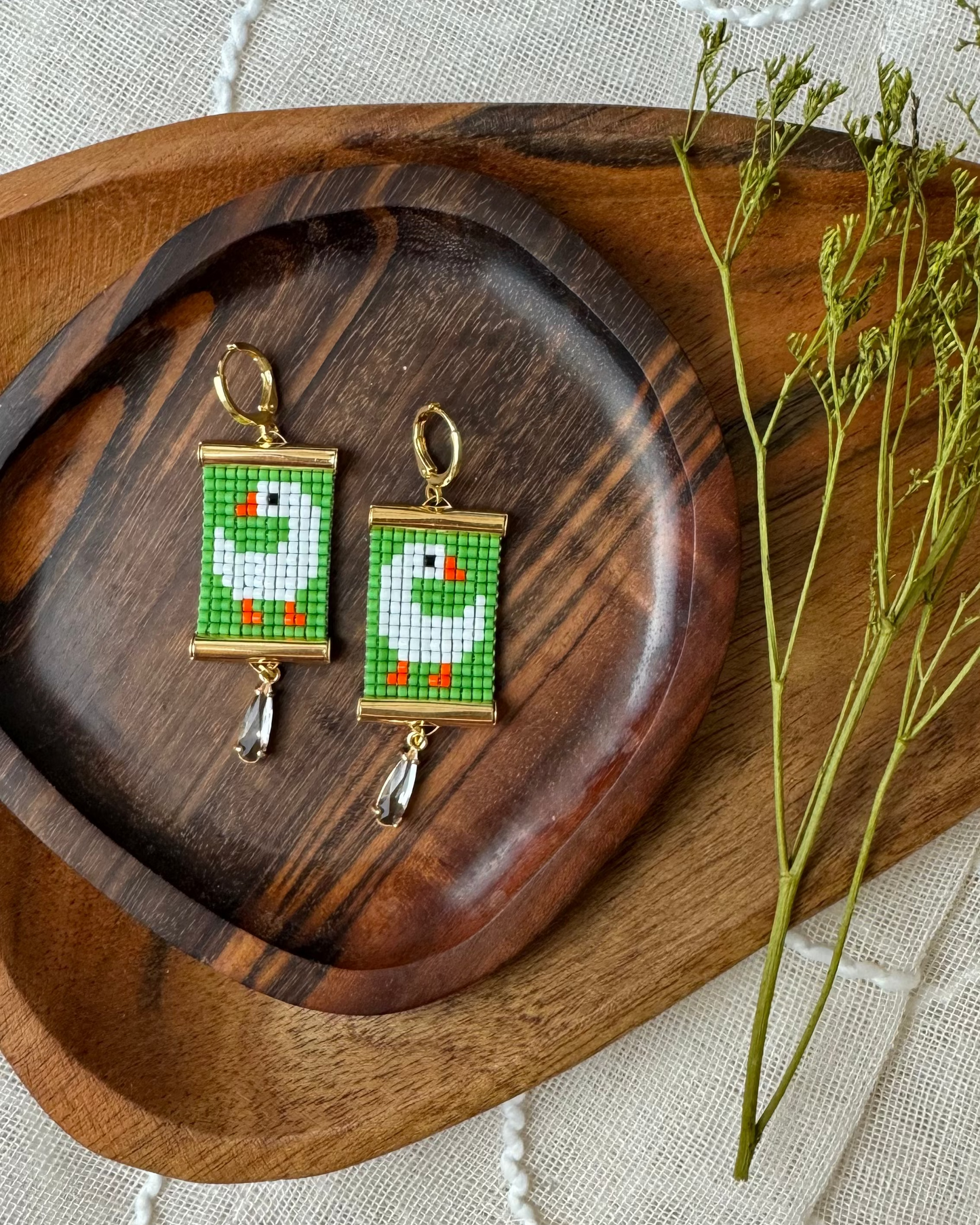 Pair of beaded earrings with green and white goose design on a wooden tray