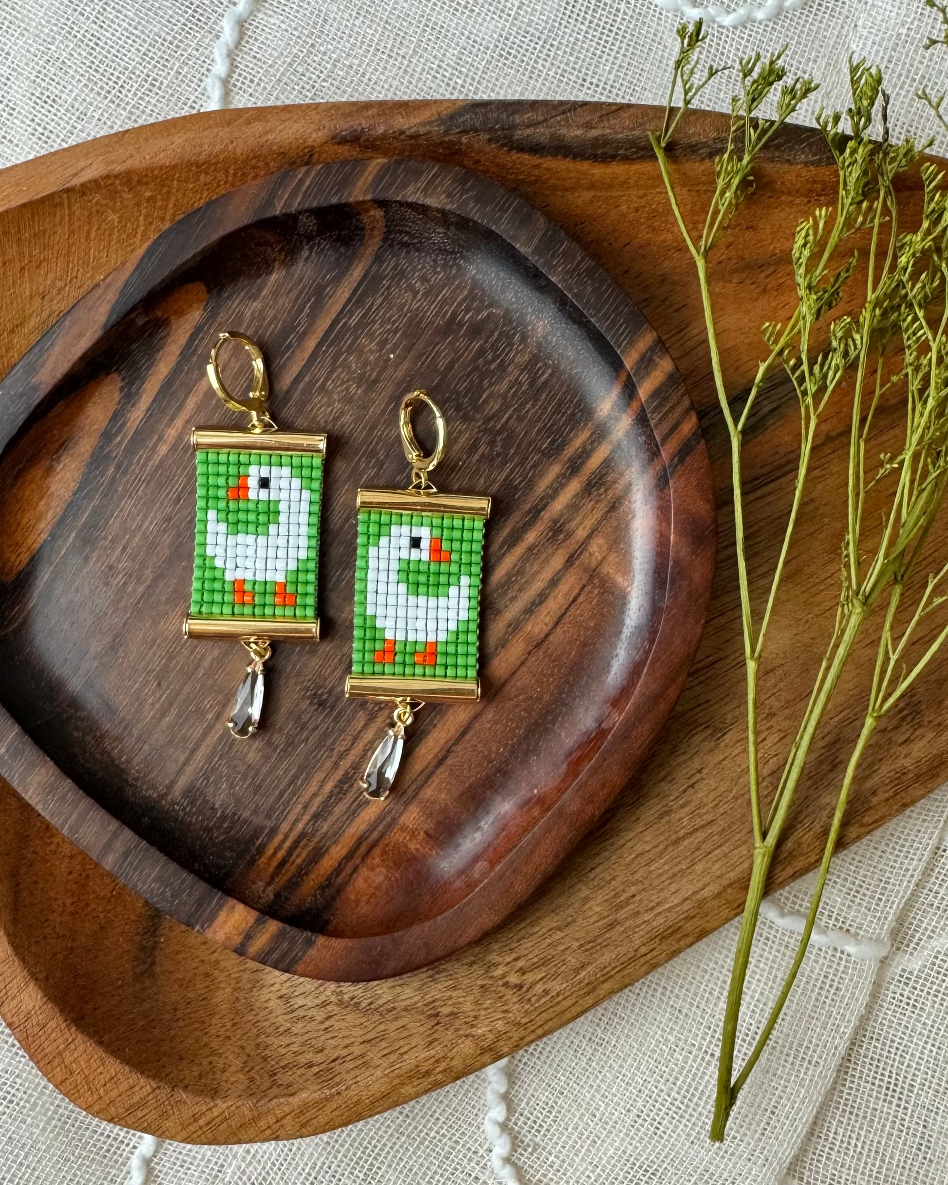 Pair of beaded earrings with green and white goose design on a wooden tray