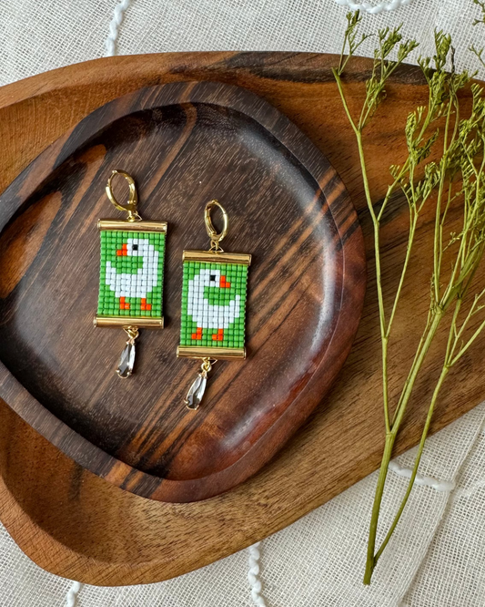 Pair of beaded earrings with green and white goose design on a wooden tray
