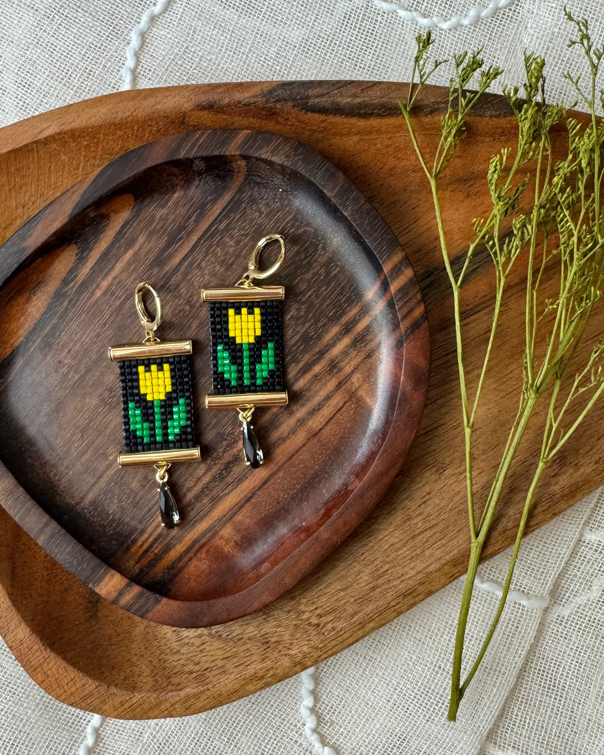 Pair of beaded earrings with tulip design on a wooden tray with a white fabric background