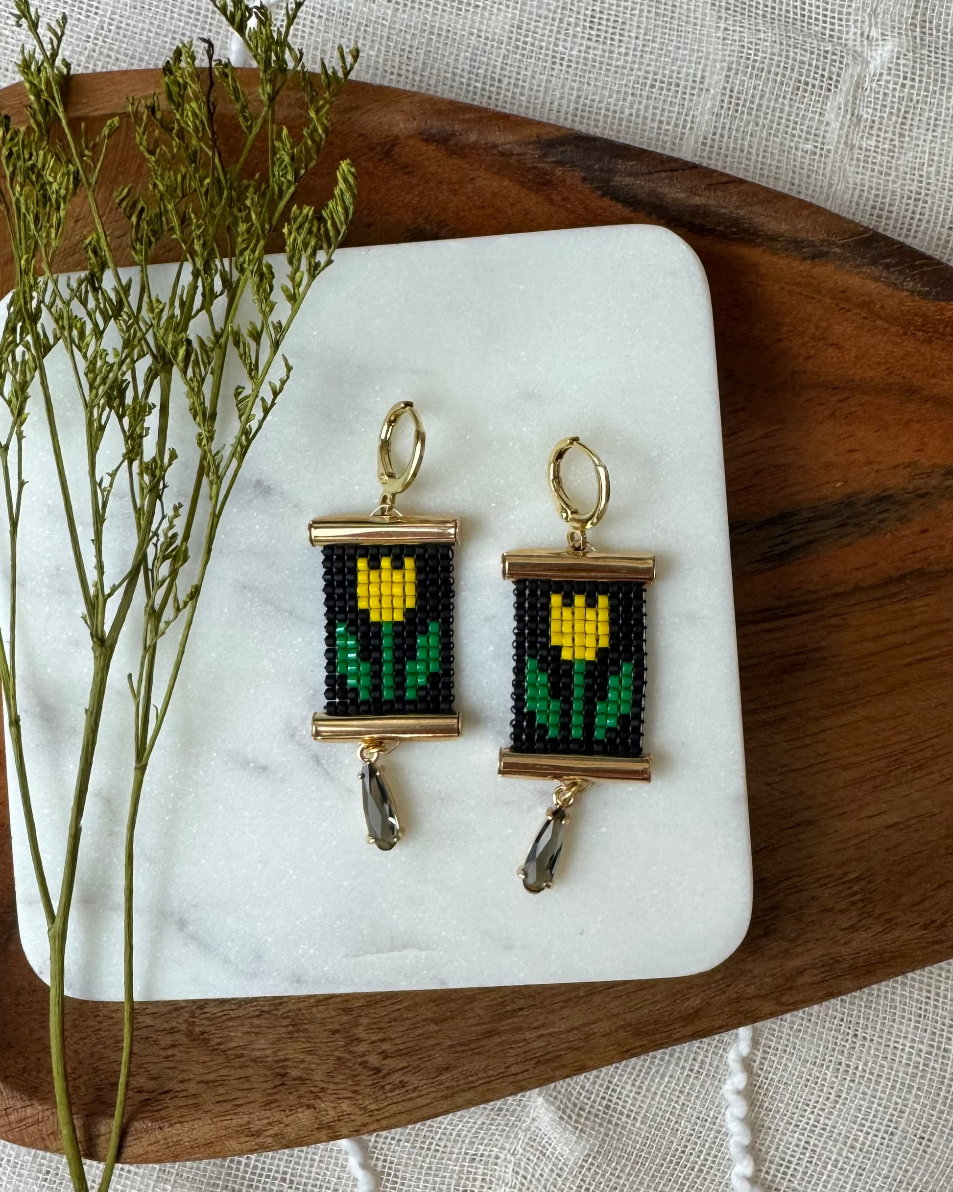 Beaded earrings on a marble stone with dried plants and a wooden board.