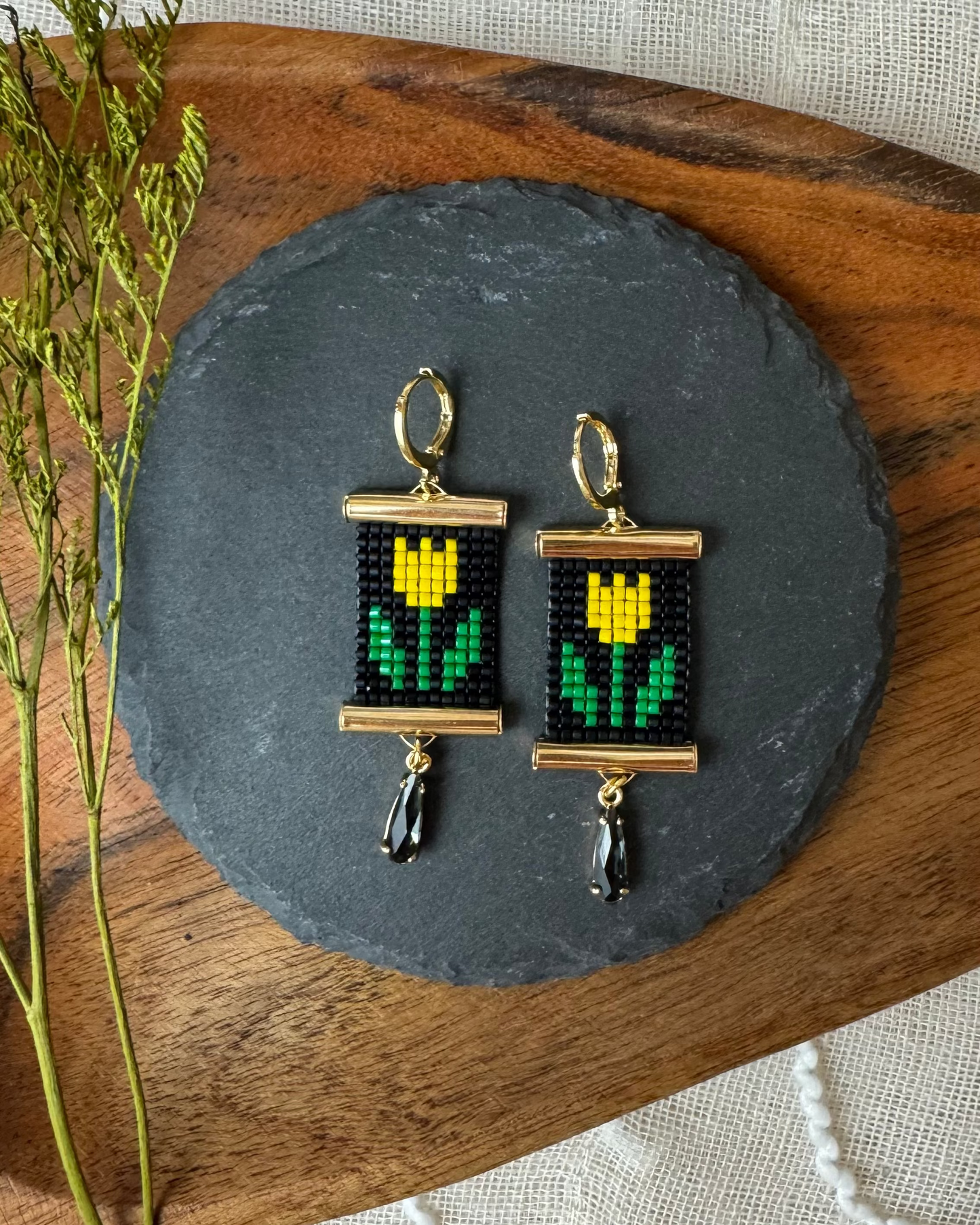 Pair of beaded earrings on a dark slate stone with a wooden base.