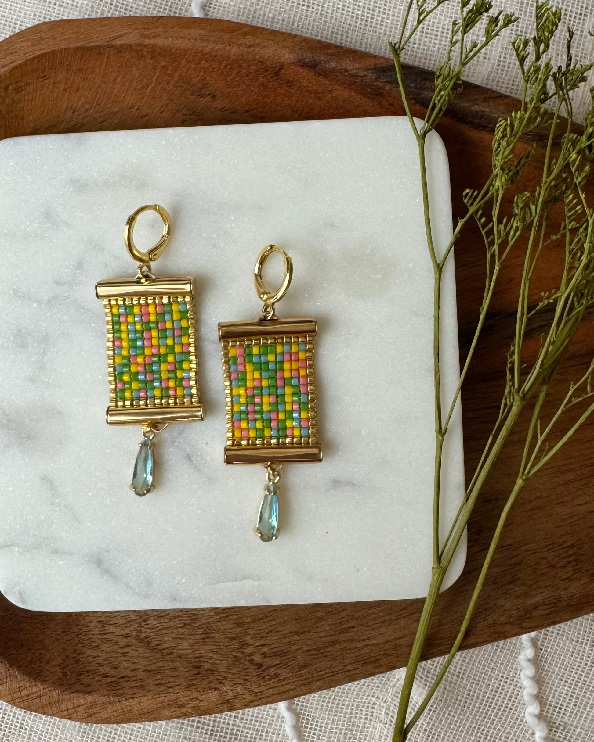 Colorful beaded earrings on a wooden tray with a white cloth background