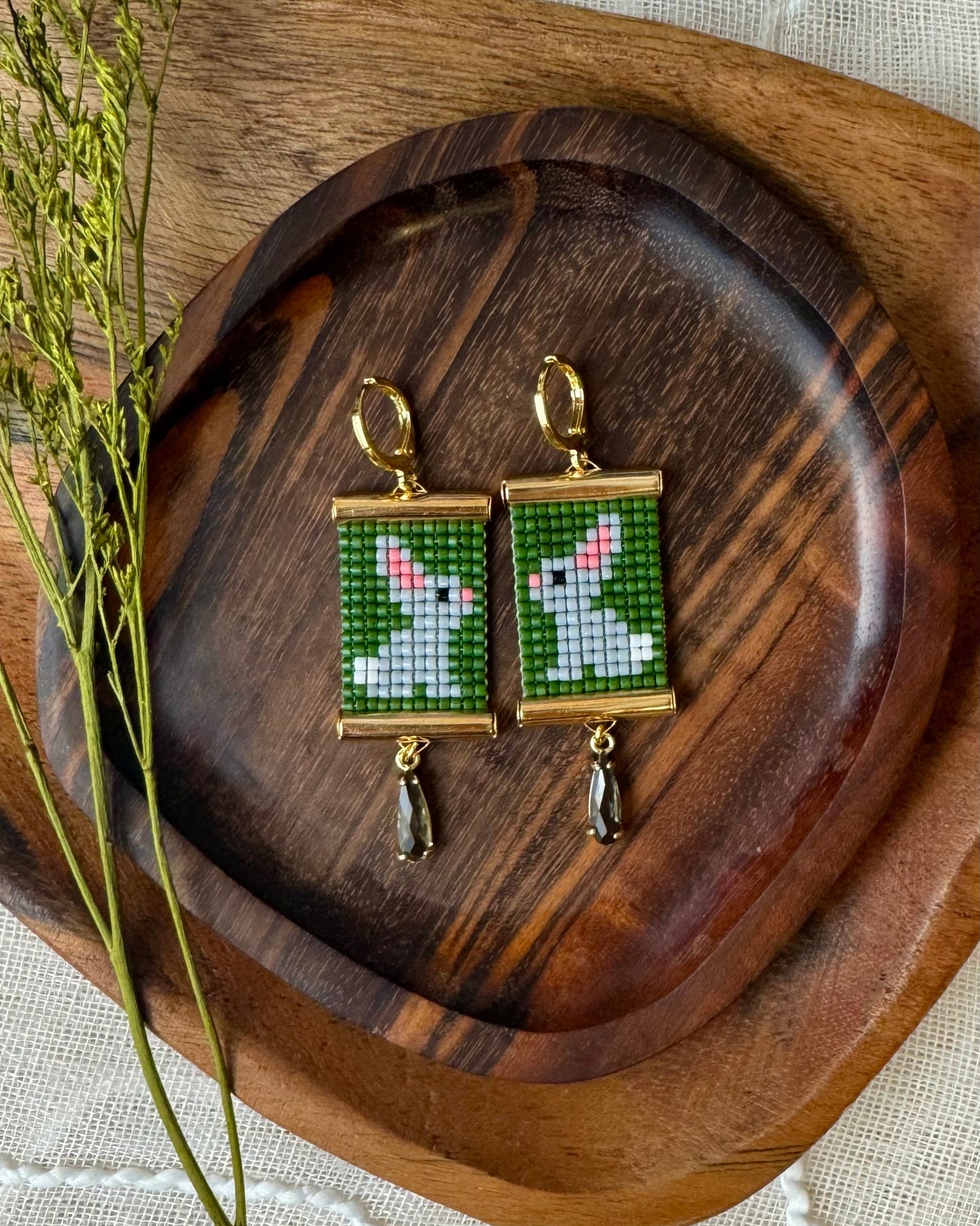 Beaded bunny earrings on a wooden tray with dried plants.