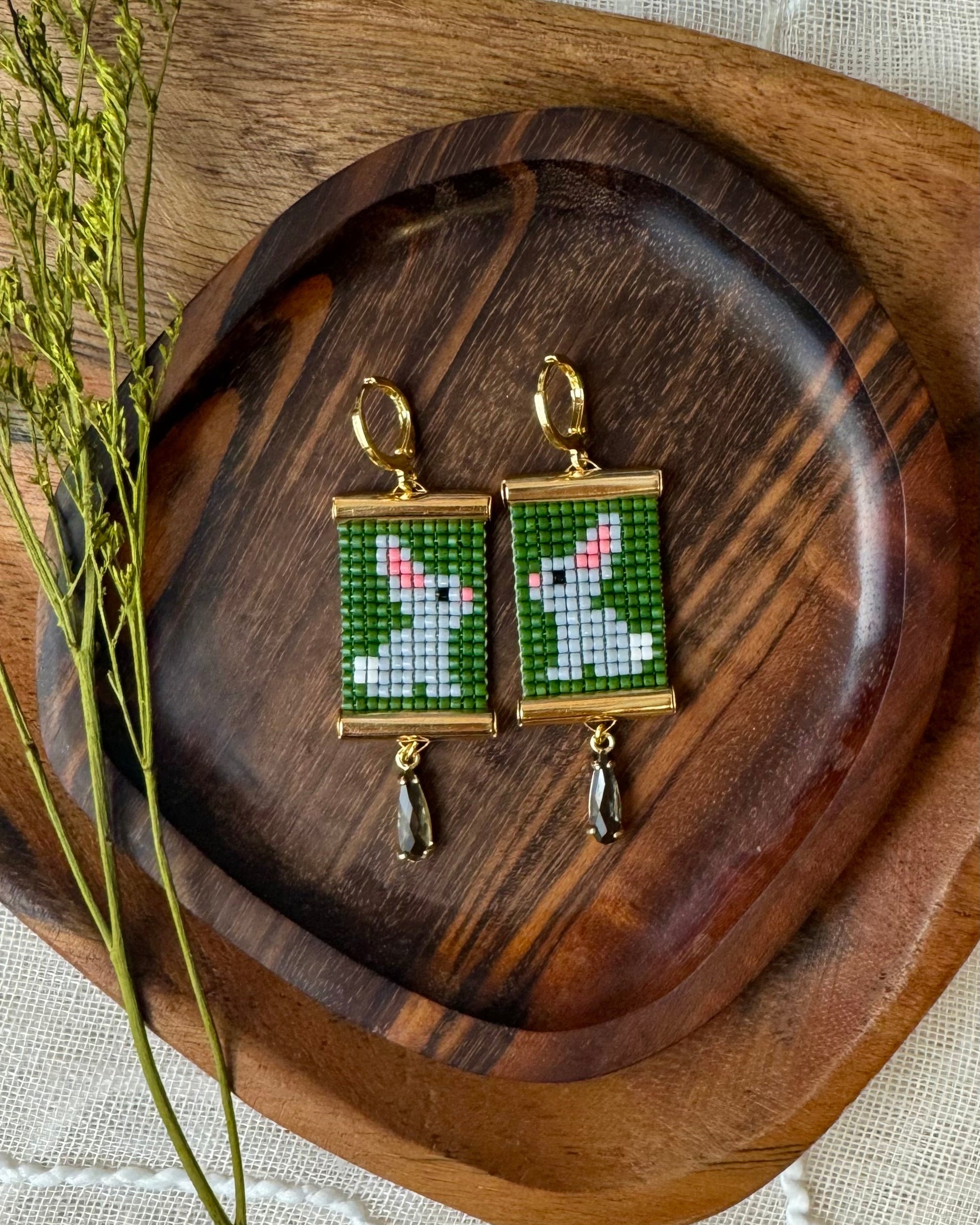Beaded bunny earrings on a wooden tray with dried plants.