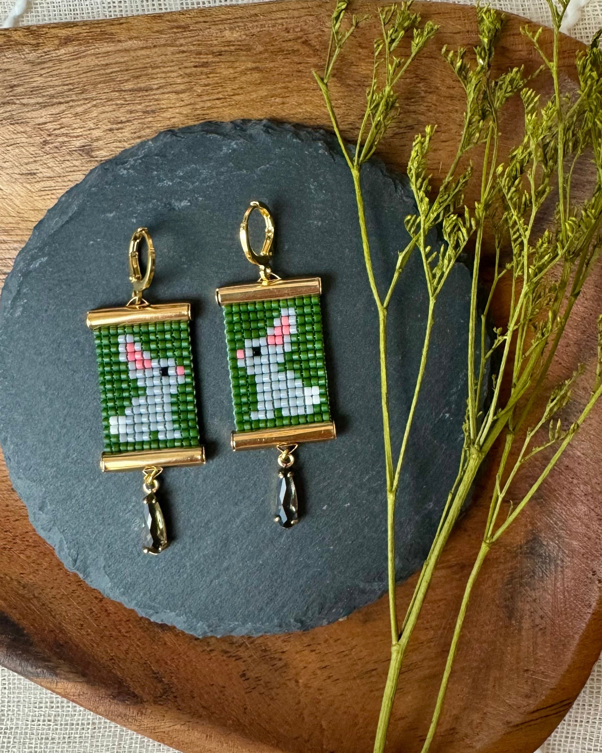 Pair of earrings with beaded bunny designs on a wooden plate.