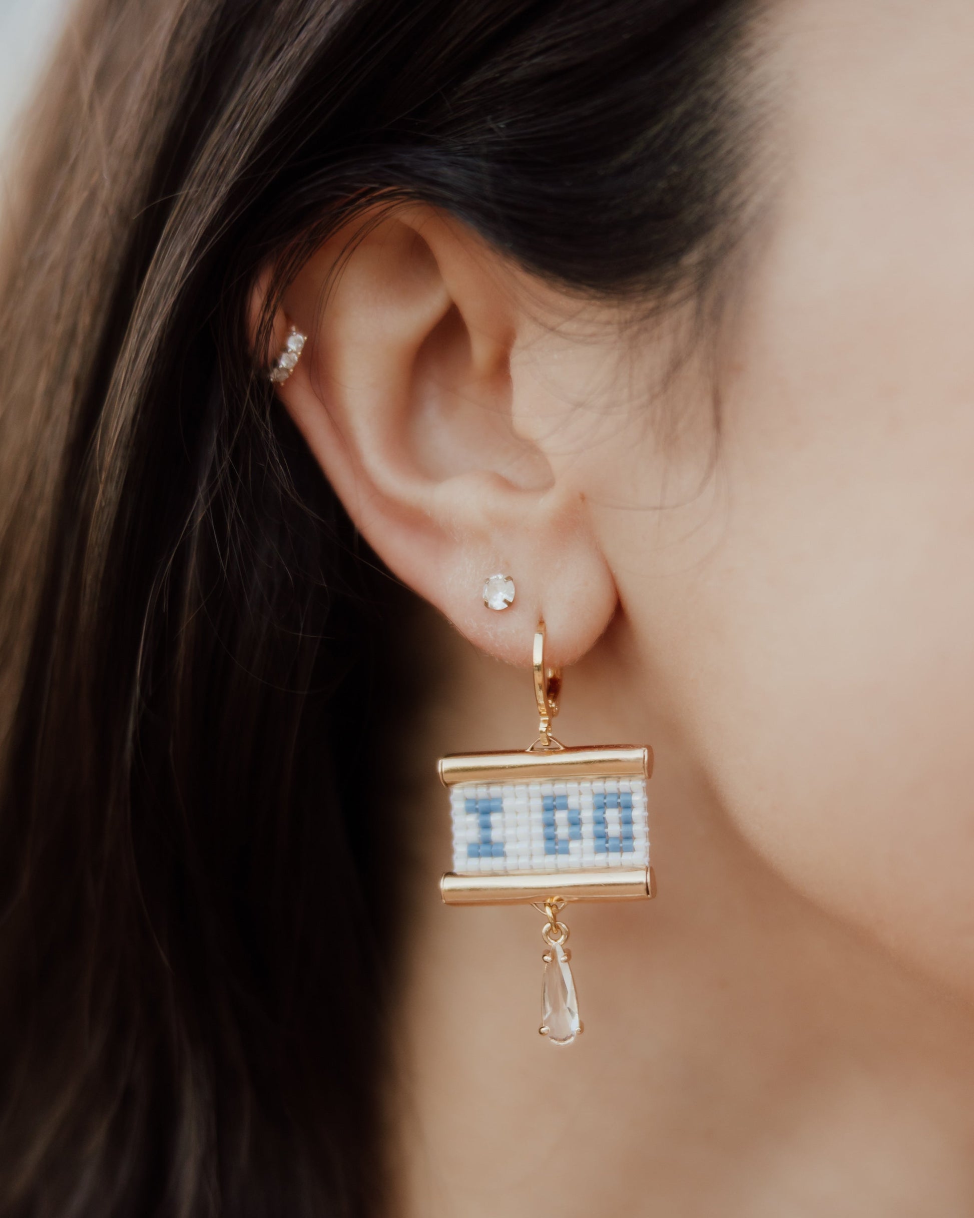 Close-up of a person wearing a gold 'I Do' earring with a clear gemstone.